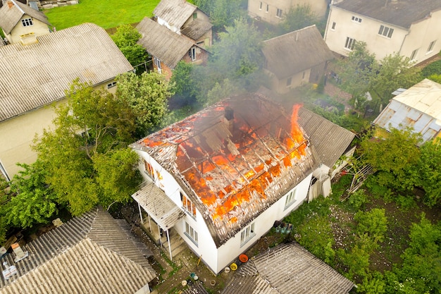 Vista aérea de uma casa em chamas com chamas laranja e fumaça branca espessa.