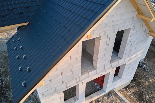 Vista aérea de uma casa inacabada com paredes de concreto leve aerado e estrutura do telhado de madeira coberta com telhas metálicas em construção.