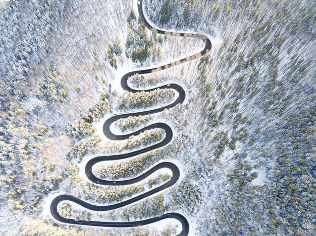 Foto vista aérea de uma estrada sinuosa em uma passagem de alta montanha através de florestas de pinheiros nevadas