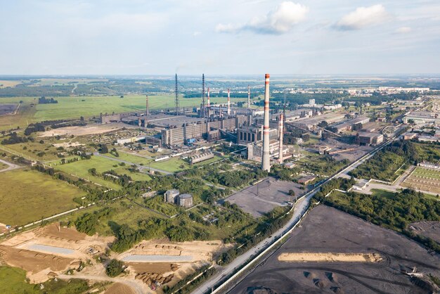 Vista aérea de uma grande planta industrial com canos altos contra uma paisagem com céu azul e nuvens Produção e poluição ambiental