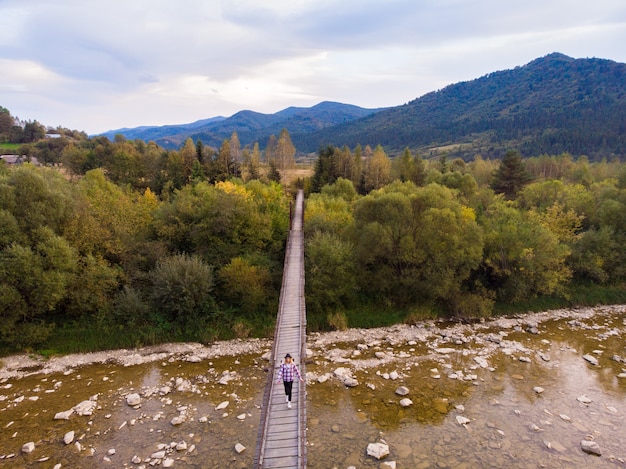 Vista aérea de uma incrível mulher viajante na ponte de madeira sobre o rio de montanhas