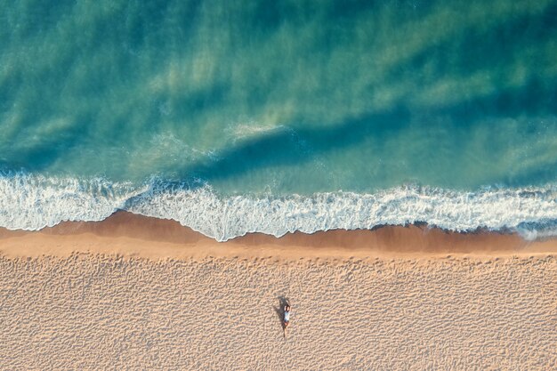 Vista aérea de uma jovem mulher com corpo bonito encontra-se sozinha na praia com águas turquesas. Viagem de férias e conceito de relaxamento vista superior