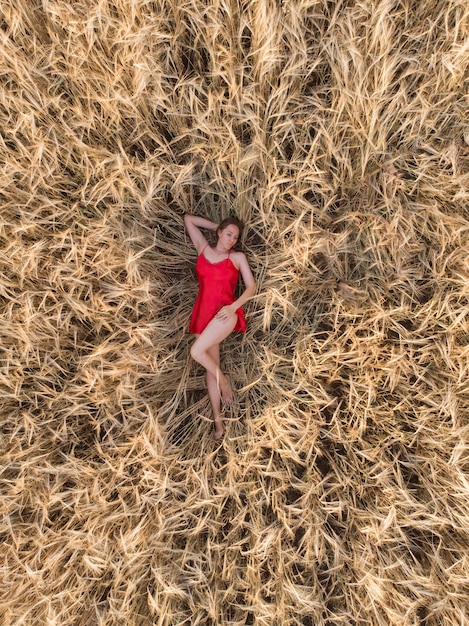 Vista aérea de uma mulher de vestido vermelho deitada no campo de trigo amarelo