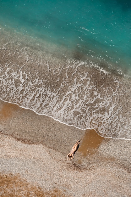 Vista aérea de uma mulher no Mar Mediterrâneo, na Turquia. Paisagem linda de verão com uma garota, água azul clara, ondas e praia em um dia ensolarado. Vista superior de um drone voador.