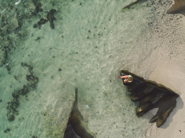 Foto vista aérea de uma mulher sentada em uma rocha na praia