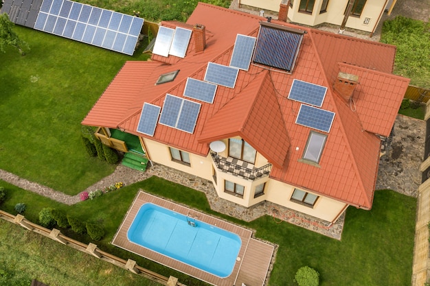 Vista aérea de uma nova casa autônoma com painéis solares e radiadores para aquecimento de água no telhado e quintal verde com piscina azul.