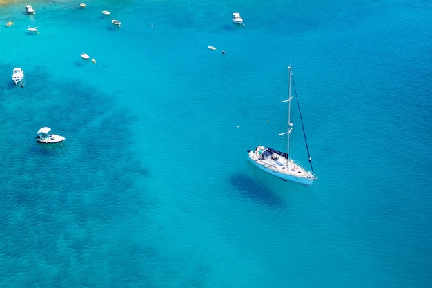 Vista aérea de veleiro e pequenos barcos ou iates nas águas azul-turquesa do mar Adriático