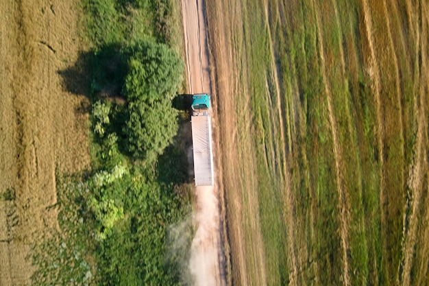 Vista aérea do caminhão de carga dirigindo na estrada de terra entre campos de trigo agrícolas fazendo muita poeira. Transporte de grãos após serem colhidos por colheitadeira durante a época de colheita.