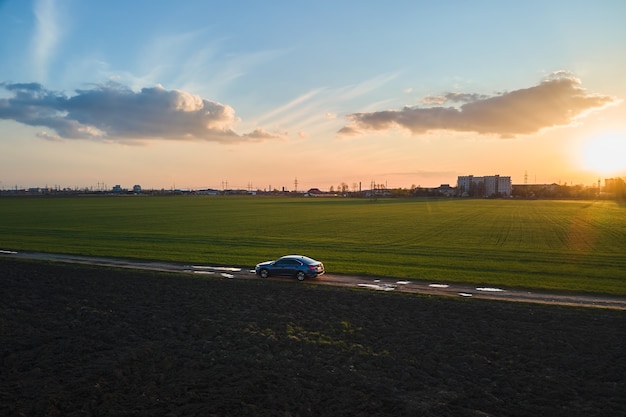 Vista aérea do carro sedan dirigindo rápido na estrada de terra ao pôr do sol. Viajando pelo conceito de veículo.