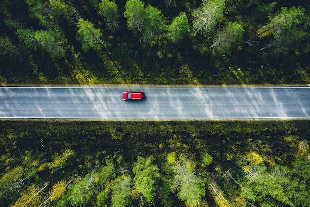 Vista aérea do carro vermelho em uma estrada rural na floresta verde na Finlândia