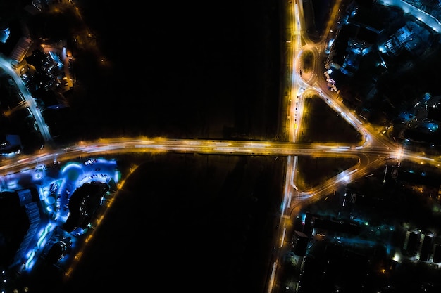 Vista aérea do cruzamento da estrada com tráfego pesado em movimento rápido à noite. Vista superior do transporte urbano. Hora do rush com luzes de trilha de carro de borrão de movimento.