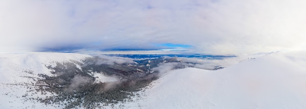 Vista aérea do deslumbrante panorama de inverno das encostas nevadas e colinas entre as exuberantes nuvens brancas