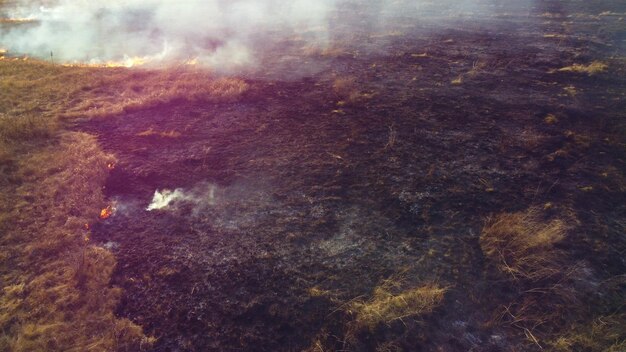 Vista aérea do drone sobre a queima de grama seca e fumaça em chamas de campo e fogo aberto