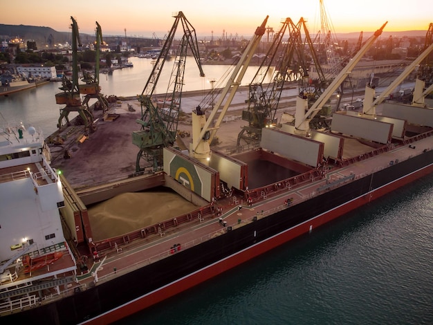 Vista aérea do grande navio de carga graneleiro é carregado com grãos de trigo no porto ao pôr do sol