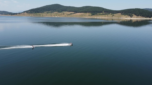 Vista aérea do homem waker esqui atrás de um barco no lago ao pôr do sol