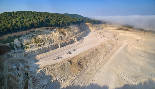 Vista aérea do local de mineração a céu aberto de extração de materiais de calcário para a indústria de construção com escavadeiras e caminhões basculantes.