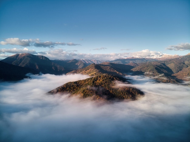 Vista aérea do mar de nevoeiro e nuvens iluminadas pelo sol nascente de neve no topo das montanhas