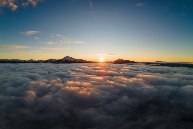 Vista aérea do nascer do sol vibrante sobre a névoa branca densa com distantes montanhas escuras dos Cárpatos no horizonte.