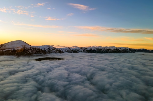 Vista aérea do nascer do sol vibrante sobre nuvens densas brancas com montanhas escuras distantes no horizonte.