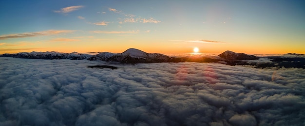 Vista aérea do nascer do sol vibrante sobre nuvens densas brancas com montanhas escuras distantes no horizonte