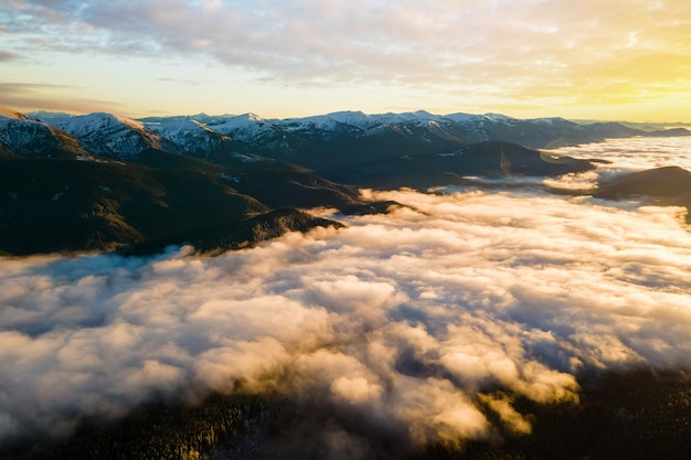 Vista aérea do nascer do sol vibrante sobre nuvens densas brancas com montanhas escuras distantes no horizonte