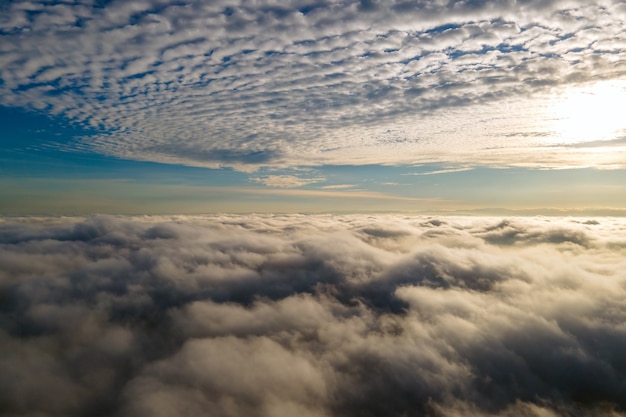 Vista aérea do pôr do sol amarelo brilhante sobre nuvens densas brancas com céu azul em cima.