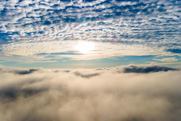 Vista aérea do pôr do sol amarelo brilhante sobre nuvens densas brancas com céu azul em cima.