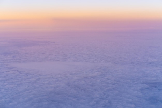 Vista aérea do pôr do sol amarelo brilhante sobre nuvens densas roxas rosa com céu azul vista de cima de um avião