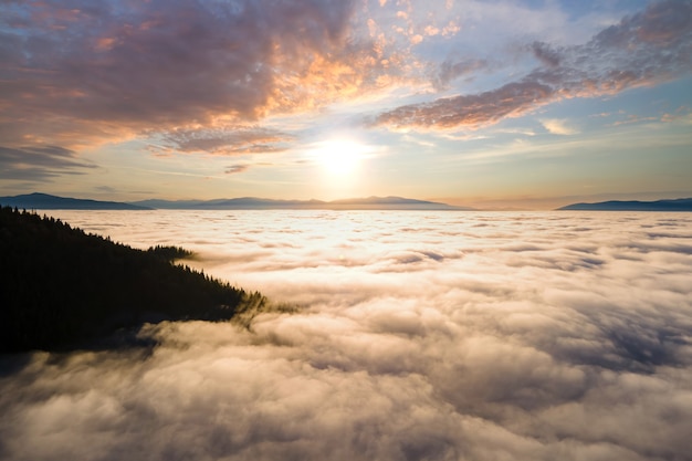 Vista aérea do pôr do sol amarelo sobre nuvens brancas e fofas com montanhas distantes no horizonte.