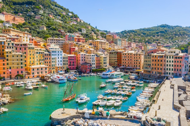 Vista aérea do porto de Camogli. Edifícios coloridos, barcos e iates ancorados na marina com água verde.