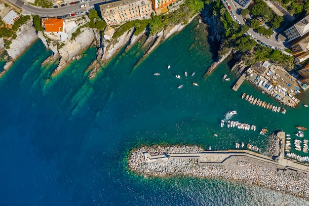 Vista aérea do porto de Camogli. Edifícios coloridos, barcos e iates ancorados na marina com água verde.