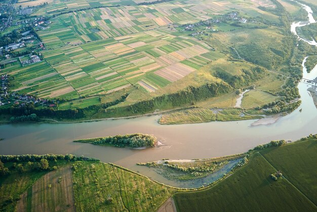 Vista aérea do rio largo que flui tranquilamente na zona rural entre campos verdes na noite de verão.