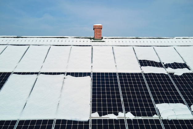 Vista aérea do telhado da casa com painéis solares cobertos de neve derretendo no final do inverno para produzir energia limpa Conceito de baixa eficácia de eletricidade renovável na região norte