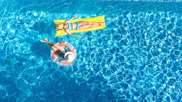 Vista aérea do zangão de crianças na piscina de cima, crianças felizes nadam no anel inflável donut e colchão, as meninas se divertem na água em férias em família no resort de férias