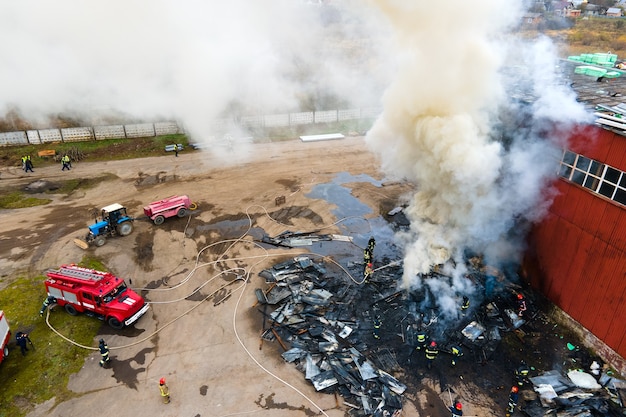 Vista aérea dos bombeiros apagando incêndio em área industrial.