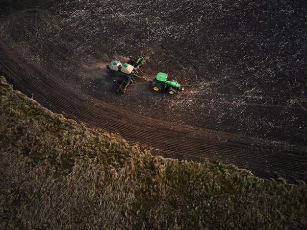 Foto vista aérea de dos modernos tractores verdes arando campos agrícolas secos y sembrando preparando la tierra para la siembra de primavera