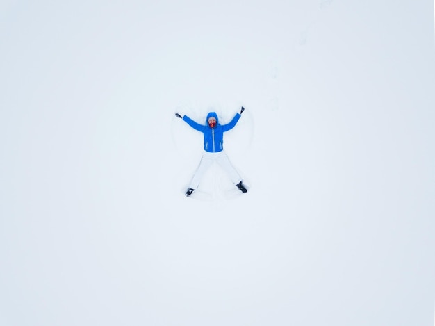 Foto vista aérea desde el dron sobre una mujer haciendo ángeles de nieve y jugando en la nieve