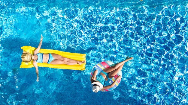 Vista aérea drone de crianças na piscina de cima, crianças felizes nadam no anel inflável donut e colchão, as meninas se divertem na água em férias em família no resort de férias