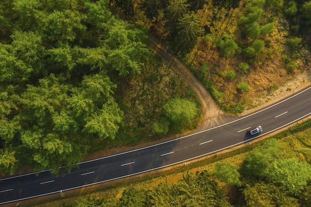 Vista aérea de drones del bosque verde. Camino con coche en el bosque desde arriba. Fondo de transporte.