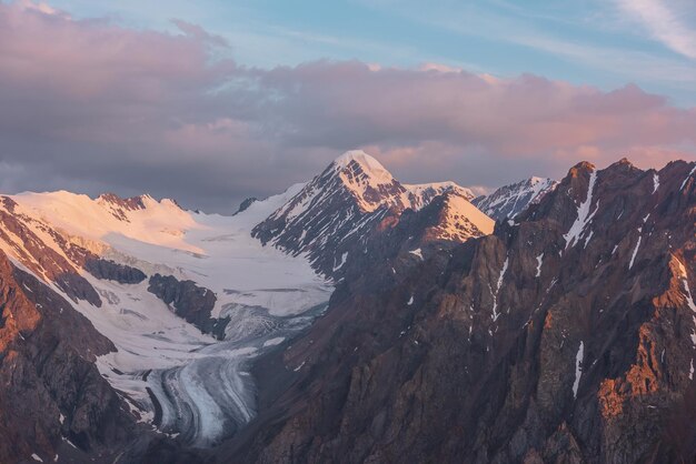 Vista aérea escénica de altas montañas nevadas temprano en la mañana al amanecer Impresionante paisaje con pináculo dorado iluminado por el sol en el cielo nublado al amanecer Paisaje matutino con pico de montaña nevada a la luz del sol dorado