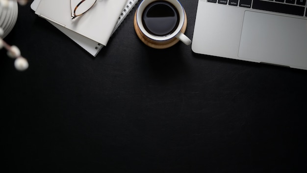 Vista aérea del espacio de trabajo con computadora portátil, cuadernos, anteojos, taza de café