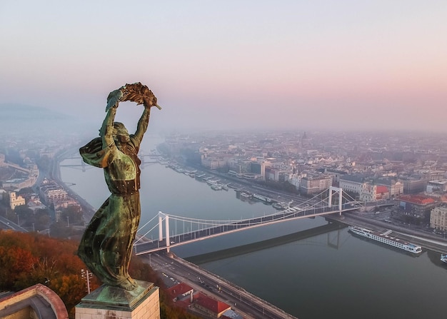 Vista aérea de la Estatua de la libertad con el puente Elisabeth y el río Danubio tomadas desde la colina Gellert al amanecer en la niebla en Budapest Hungría