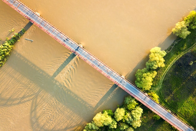 Vista aérea de un estrecho puente de carretera que se extiende sobre un río ancho y fangoso