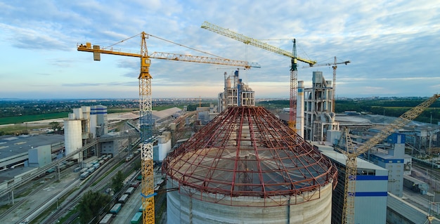 Vista aérea de la fábrica de cemento en construcción con alta estructura de planta de hormigón y grúas torre en el área de producción industrial. Concepto de industria global y fabricación.