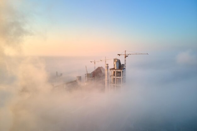 Vista aérea de la fábrica de cemento con estructura de planta de hormigón alta y grúa torre en el sitio de producción industrial en la mañana brumosa. Concepto de industria global y fabricación.