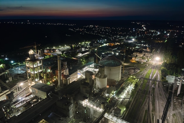 Vista aérea de la fábrica de cemento con estructura de planta de hormigón alta y grúas torre en el área de producción industrial por la noche. Concepto de industria global y fabricación.