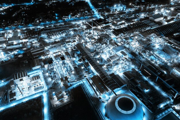 Vista aérea de la fábrica industrial de luz azul con refinería química y material de construcción que brilla intensamente en la noche