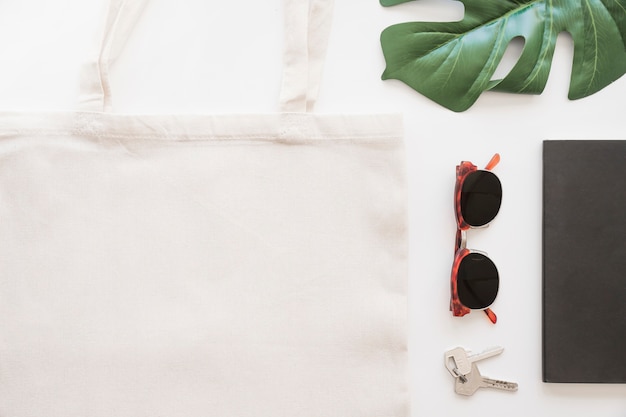 Vista aérea de gafas de sol, llave, bolso de mano y hoja de monstera sobre fondo blanco