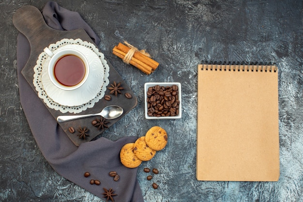 Vista aérea de galletas caseras, canela, limones y una taza de té en la tabla de cortar de madera, granos de café, cuaderno sobre fondo de hielo