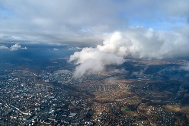 Vista aérea desde gran altura de una ciudad lejana cubierta de cúmulos hinchados que vuelan antes de la tormenta Punto de vista del avión del paisaje en tiempo nublado